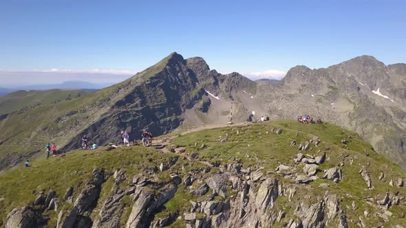 Drone orbiting high mountain peak with hikers resting after ascent to the summit. Rugged remote land