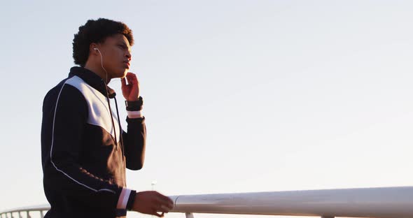 African american man putting earphones on during exercise outdoors by seaside