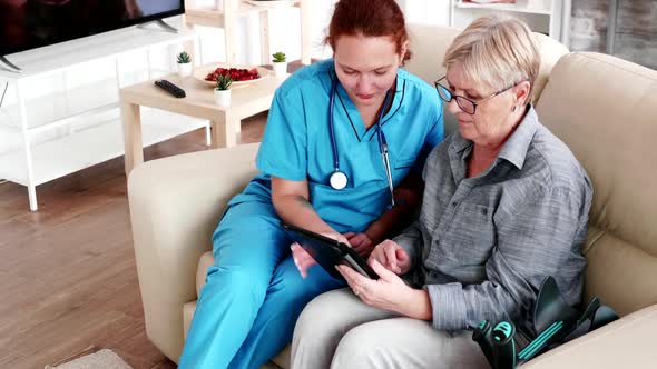 Female Nuse Helping Senior Elderly Retired Woman How To Use Her Tablet Computer