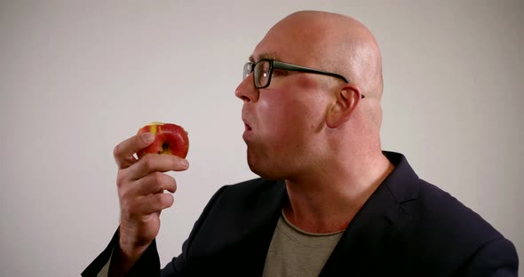 Portrait a Bald Man Wearing Glasses and a Suit on a Vegetarian Raw Food Diet Bites and Chews a Red