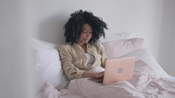 Portrait of Young Confident Woman Typing on Laptop Keyboard Lying in Bed in the Morning