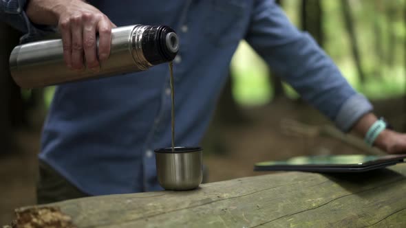 Hiker pouring coffee in cup in the forest