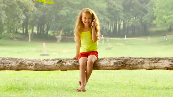 Adorable Little Girl Talking on Smartphone Sitting in a Tree