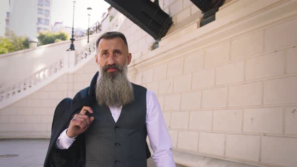 Handsome Bearded Mature Man in Suit Walking Outdoors on Modern Building Background During Sunny Day