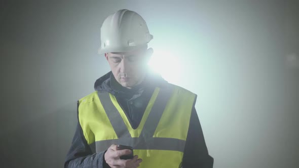 Portrait of the Man in the Builders Uniform and Helmet Texting on Cell Phone in Front of the Black