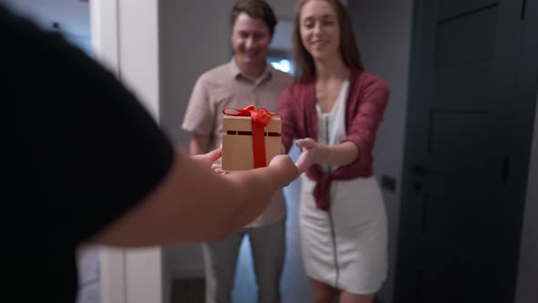 Rack Focus From Gift Box in Female Hands to Apartment Owners Smiling Greeting Guest Indoors in Slow