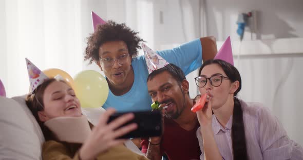 Young Injured Female with Neck Brace Taking Birthday Selfie with Friends in Hospital Ward