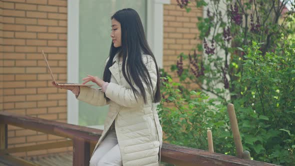 Side View of Young Woman Typing on Laptop Keyboard Laughing Sitting on Sunny Porch on Backyard