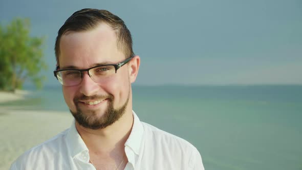 Portrait of a Young Man on a Tropical Beach. In an Easy Shirt, He Smiles and Looks Into the Camera