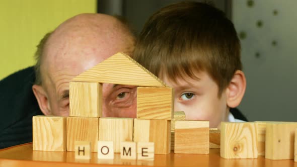 The inscription home from wooden cubes. Caucasian grandfather over 70 years old with a grandson 7 ye