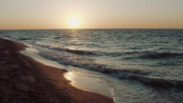 Aerial View Above Water of Nesting Small Waves Against Sandy Shore Against the Backdrop of Sunset