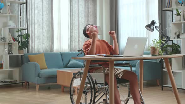 Young Asian Boy Sitting In A Wheelchair While Using Laptop Computer And Celebrating At Home