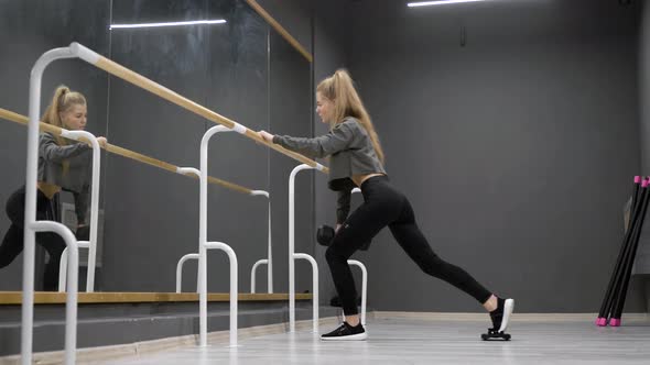 Sexual Woman Is Training Alone in Fitness Hall, Holding Dumbbell in Hand and Crouching in Front of