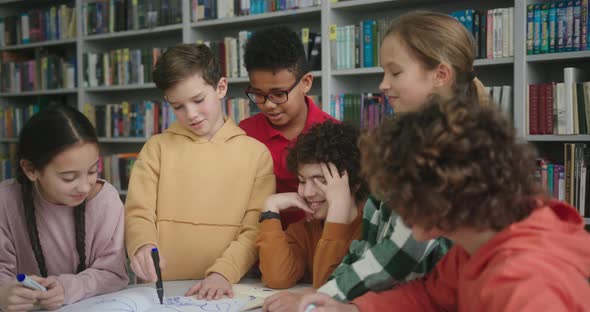 Kids Draw with Markers in Sketchbook at Table in Library