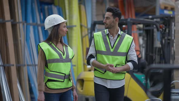 Middle Eastern Man and Caucasian Woman Walking in Warehouse Talking