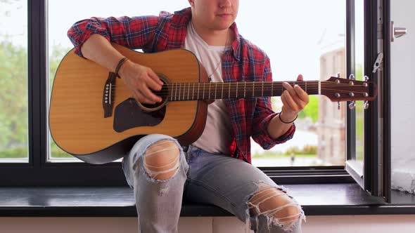 Young Man Playing Guitar Sitting on Windowsill