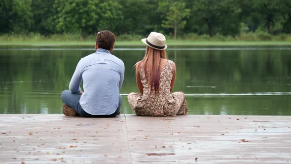 Couple sitting at the lake sitting on the edge of a wooden jetty.