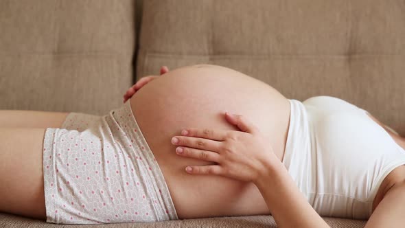 A Caring Mother Strokes a Naked Pregnant Tummy with Two Hands, on Light Room. A Pregnant Woman