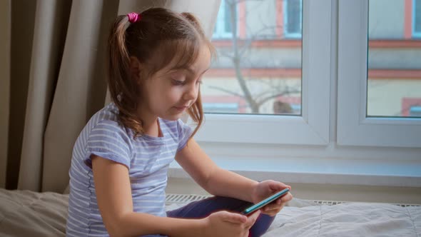 Portrait of a Child Looking at a Mobile Phone at Home