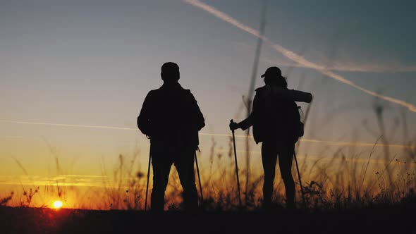 Silhouettes of Two Hikers with Backpacks Enjoying Sunset View From Top of a Mountain. Enjoying the