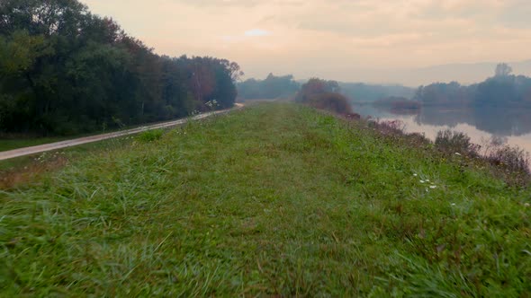 Drone shot traveling along a grassy hill with a nearby reflective lake on a foggy autumn morning