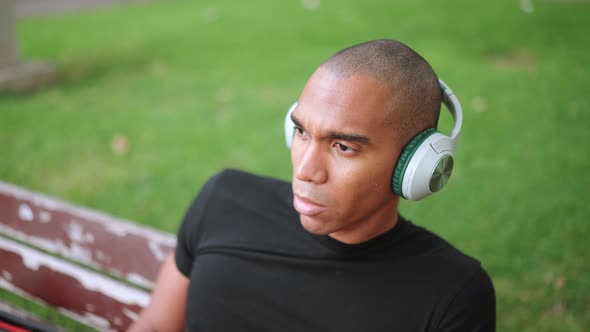 Confident bald African man listening music in headphones while sitting on the bench