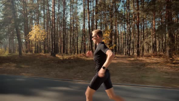 Running Man In Forest At Sunset. Runner Man Fit Athlete Legs Jogging On Trail Ready To Triathlon.