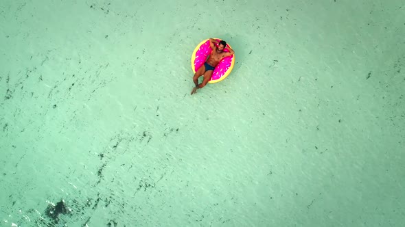 Aerial view of man floating on inflatable donut mattress, relaxing.