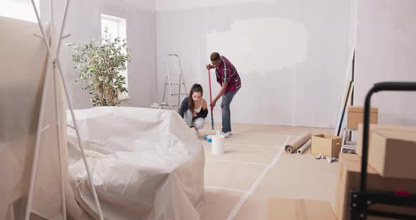 Two Young Cheerful People Working Together to Finish an Apartment Hold Paint Rollers in Their Hands