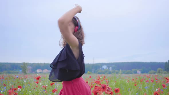 Pretty Young Woman Wearing Headphones Listening To Music and Dancing in a Poppy Field Smiling