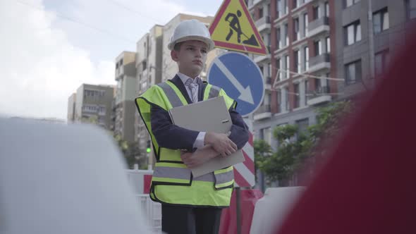 Portrait Thoughtful Little Boy Wearing Safety Equipment and Constructor Helmet Holding Building Plan