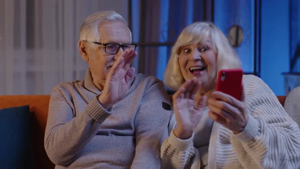 Smiling Senior Couple Grandmother Grandfather Making Video Call Online on Mobile Phone at Home Sofa