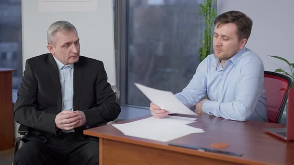 Joyful Senior Disabled Man and Young Guy Giving Highfive Discussing Project in Office