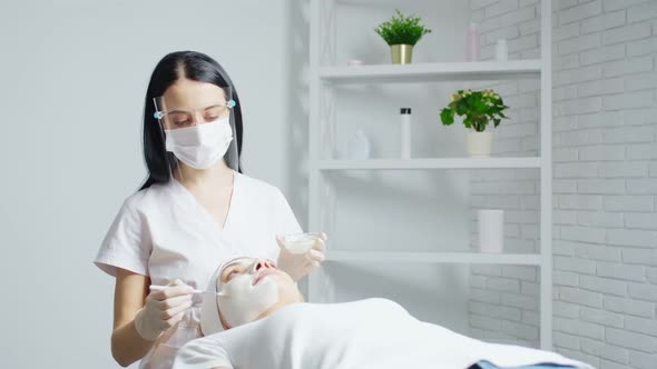 Beautician Applying Special Facial Mask for Young Woman