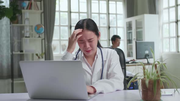 Young Asian Woman Doctor Is Using Laptop Computer And Headache In Workplace. Medical Concept