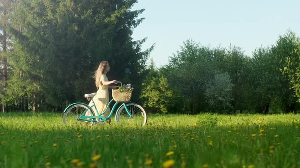 Happy Young Woman Walk With a Bike With Basket of Flowers on the On Countryside Road At Summer at