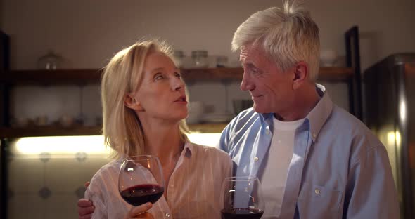 Senior Couple in Love in Kitchen Talking and Drinking Red Wine