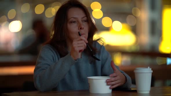 Portrait of a Middle-aged Woman in a Sweater, She Is Sitting in a Cafe, Eating From Disposable