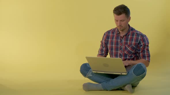 Attractive Young Man Chatting with Friends on Computer While Sitting on the Floor