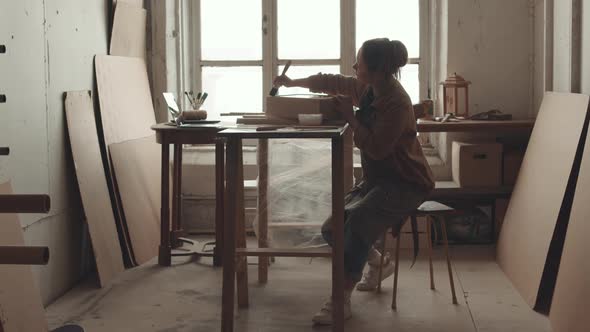 Young Craftswoman Painting Wooden Drawer in Workshop