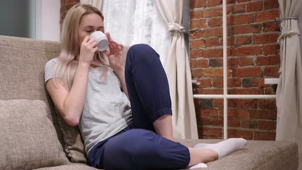 Young Woman Drinking Coffee From Cup Sitting on Sofa