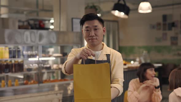 Young Asian Waiter Holding Paper Bag with Takeaway Meal