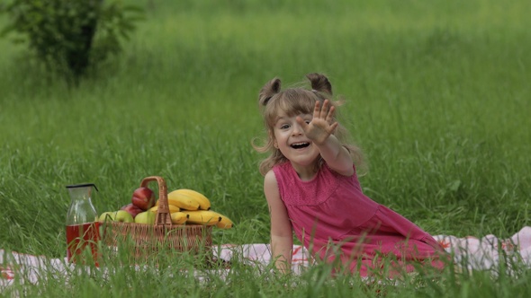 Weekend at Picnic. Lovely Caucasian Child Girl on Green Grass Meadow Sit on Blanket Waving Her Hands