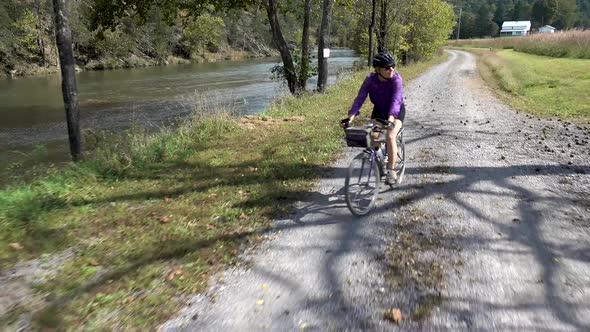 Pretty, mature woman on a mountain bike riding on a gravel road with a river on one side and farmlan