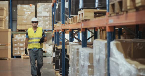 Logistics worker wearing a helmet working in a large warehouse checking inventory