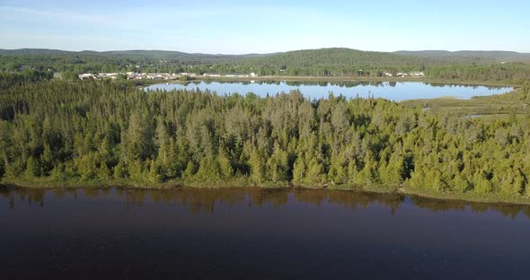 Aerial shot tilting down flying over a lake coastline towards a beautiful forest in northern Ontario