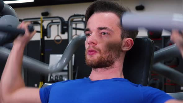 A Young Fit Man Trains on a Machine in a Gym - Face Closeup