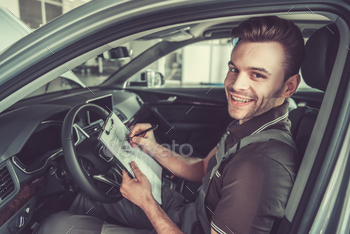 notes, looking at camera and smiling while examining car in auto service