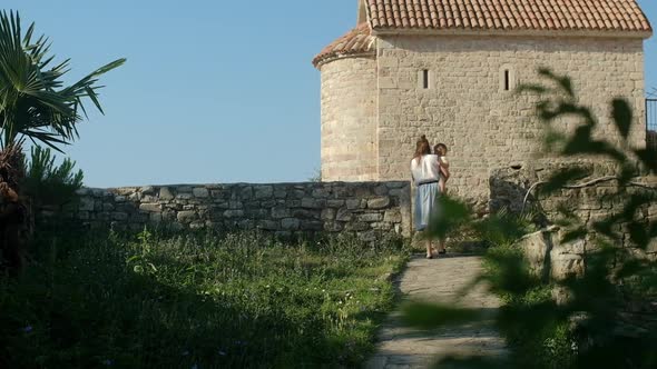 Back view through green plants on woman with child walking in Old Town in Europe