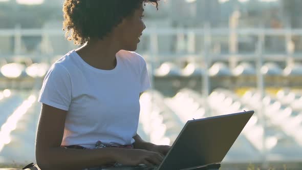 Young Afro-American Woman Working on Laptop, Sitting on Grass in City Park